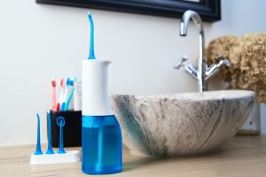 image of waterpik next to sink, a dental tool used to make flossing hard to reach places and restorations like dental implants easier